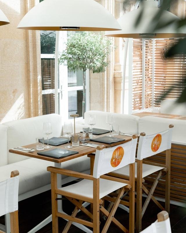 Table dressée sous la véranda de La Mado : plateau en bois, verres à vin, olivier en pot et mur de pierre d'Aix.