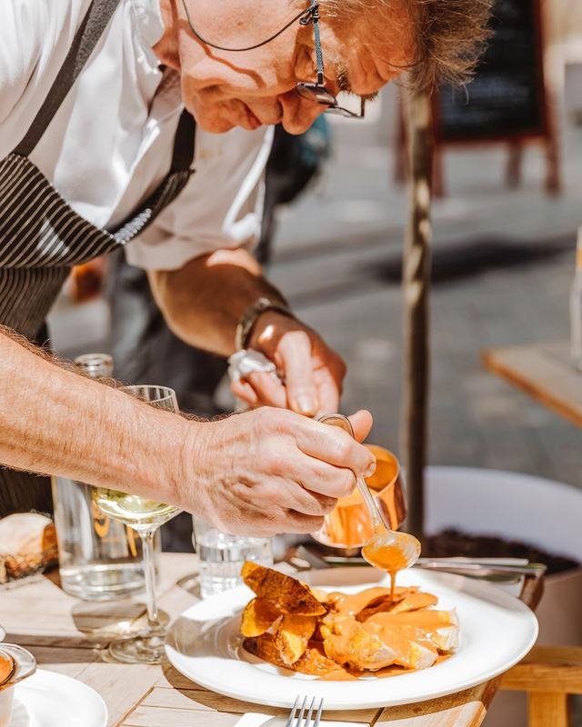Le chef nappe un plat de sauce directement à la table, en terrasse.